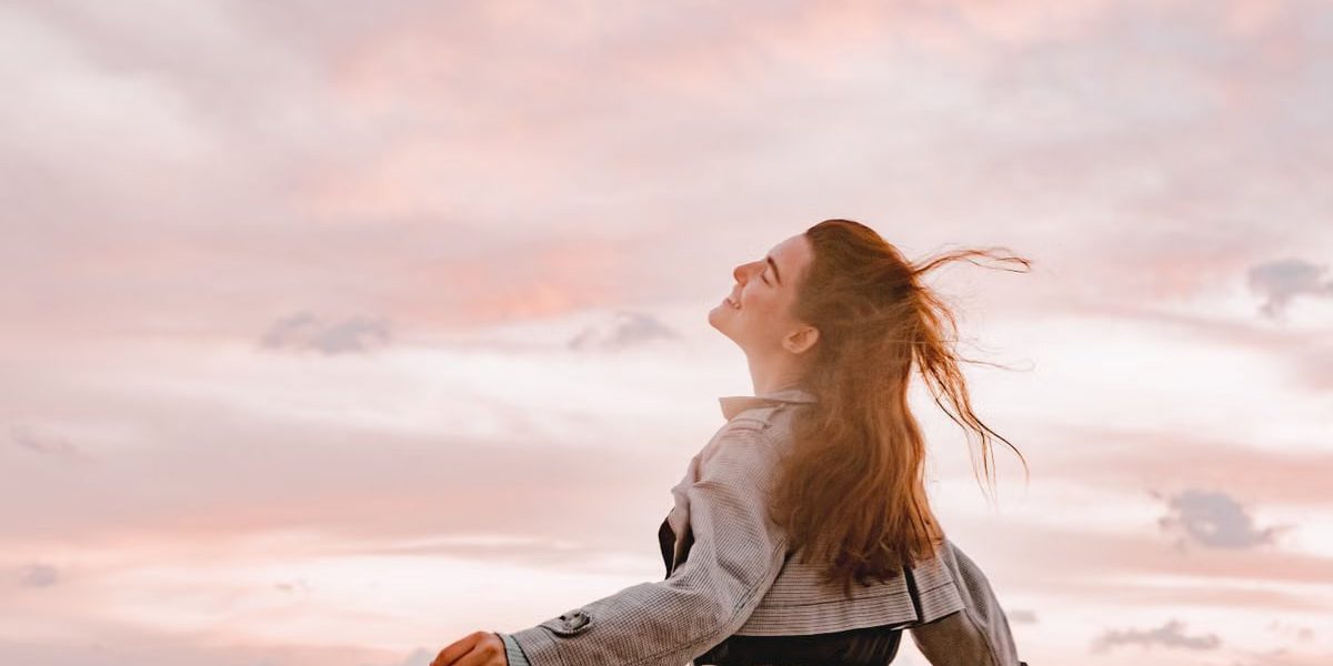 A woman joyfully embraces the sunset with arms spread in freedom, capturing serenity in nature.