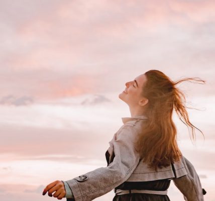 A woman joyfully embraces the sunset with arms spread in freedom, capturing serenity in nature.