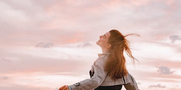 A woman joyfully embraces the sunset with arms spread in freedom, capturing serenity in nature.